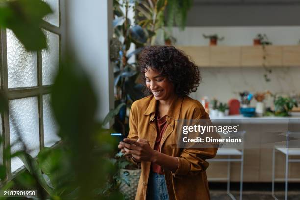 giovane donna, usando, telefono cellulare, e, sorridente, in, lei, appartamento pieno di piante - mondo naturale foto e immagini stock