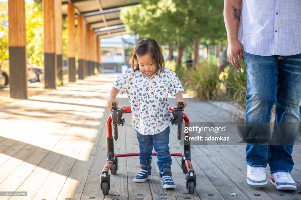 Hispanic Boy with Down's Syndrome Using Walker with Dad