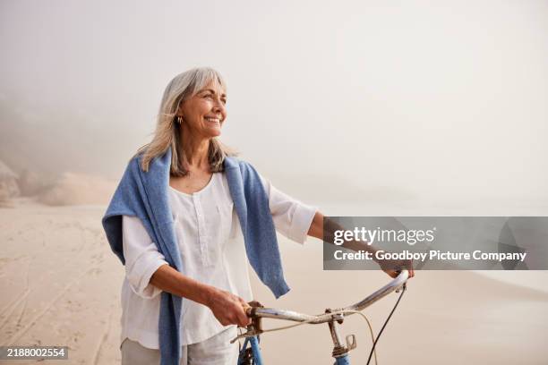 mujer mayor activa de unos 60 años empujando la bicicleta en la playa de arena - encuadre cintura para arriba fotografías e imágenes de stock