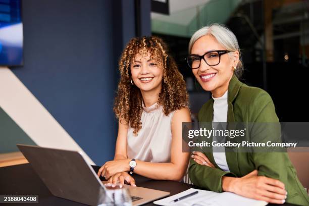 portrait of two female business colleagues sitting at desk with laptop, smiling towards camera - mentor imagens e fotografias de stock