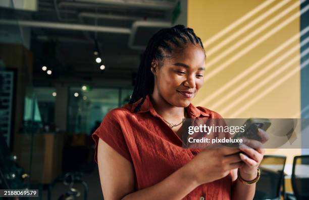 young businesswoman using mobile phone, smiling and standing in modern office - employee mobile phone stock pictures, royalty-free photos & images