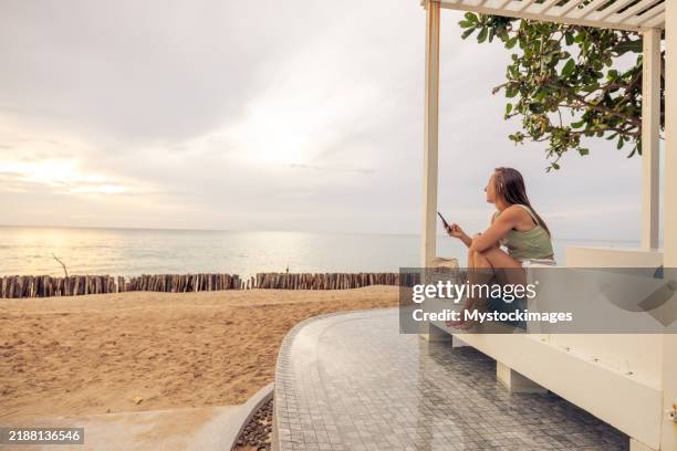 femme se relaxant au bord de la plage sur un banc à l’aide d’un smartphone - cabine de plage photos et images de collection