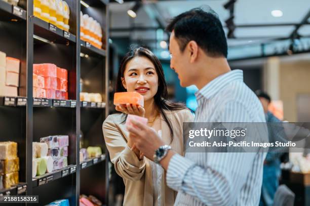 asian couple shopping for handmade soap. hand with lavender herbal soap on the background of shelves with a range of products for body care and bathroom cosmetics. - we love customers stock pictures, royalty-free photos & images