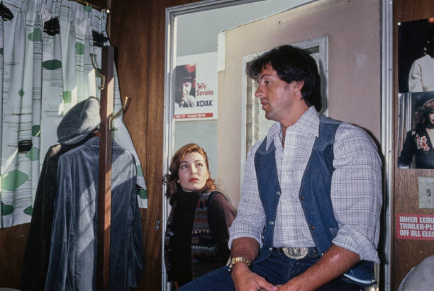 American actor Sylvester Stallone, wearing a denim waistcoat over a checked shirt, as he sits for a sculptor creating a clay bust of Stallone as a...