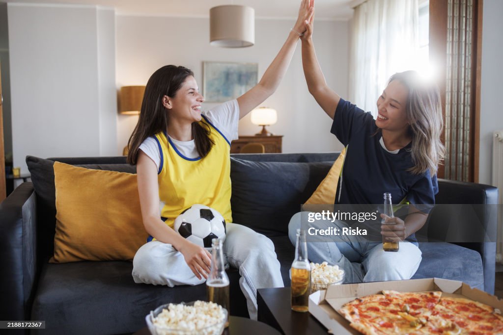 Zwei Freunde feiern einen Fußballsieg mit Pizza und Getränken zu Hause