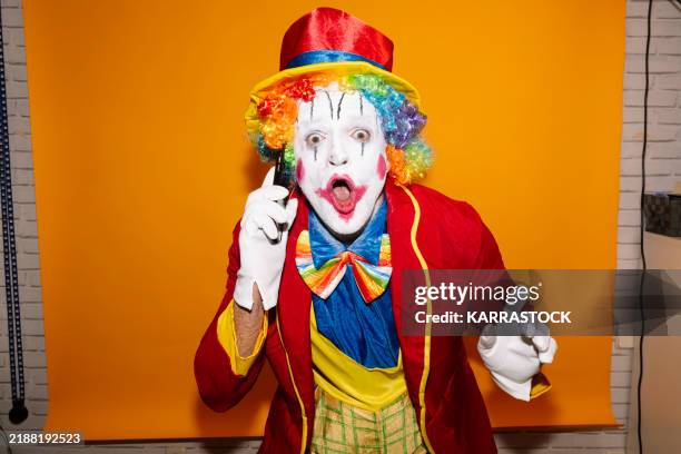 happy clown uses smartphone, vibrant yellow background. - clown stock pictures, royalty-free photos & images