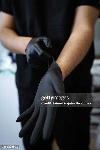 esteticista poniéndose guantes de nitrilo negro para un procedimiento - guante quirúrgico fotografías e imágenes de stock