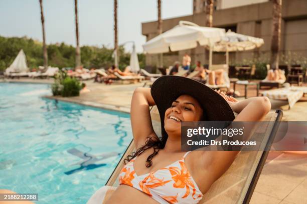 frau liegt auf sonnenliege am pool in luxushotel - schwimmbeckenrand stock-fotos und bilder
