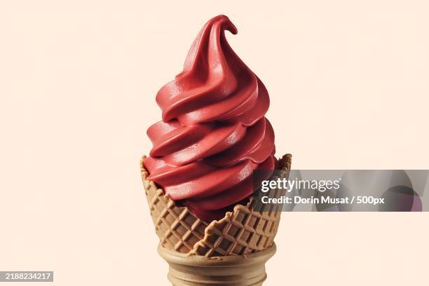 a soft serve ice cream cone with a vibrant red ice cream swirl on top - gefrorener joghurt stock-fotos und bilder