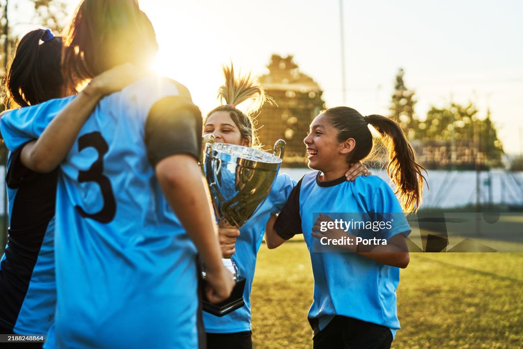 Time de futebol de adolescentes comemorando vitória com troféu