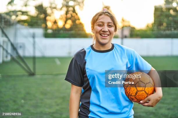 happy teenage soccer player holding ball on field - alleen één tienermeisje stockfoto's en -beelden