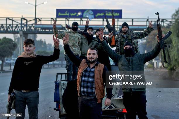 Syrian rebel fighters celebrate at the entrance of Homs province early on December 8 after rebel forces entered Syria's third city overnight. Hayat...