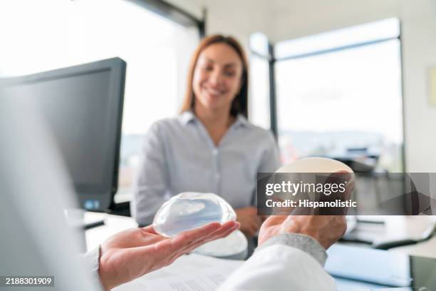 surgeon showing two breast implants to a patient interested in a breast augmentation - plastic surgery stock pictures, royalty-free photos & images