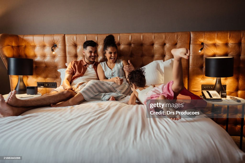 Couple playing with daughter on hotel bed