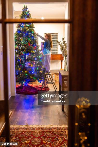 kinder, die den weihnachtsbaum durch das fenster schmücken - weihnachtsbaum schmücken stock-fotos und bilder