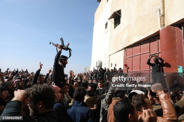 Man holds a rifle as people gather at Sednaya Prison, where thousands of people were said to be detained and tortured by the Assad regime over the...