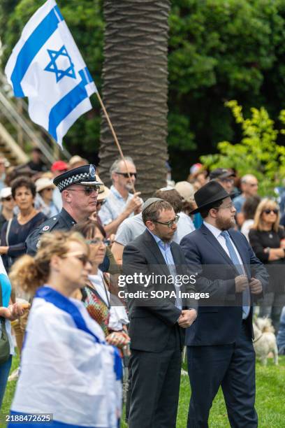 Senior police officer stands with members of the Jewish community as protesters hold signs and wave Israeli flags during a demonstration near the...