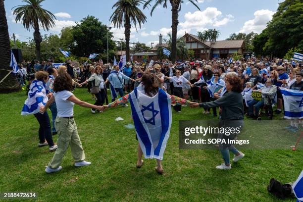 Protesters hold signs and wave Israeli flags as others dance during a demonstration near the burnt Adass Israel Synagogue, calling for justice and...