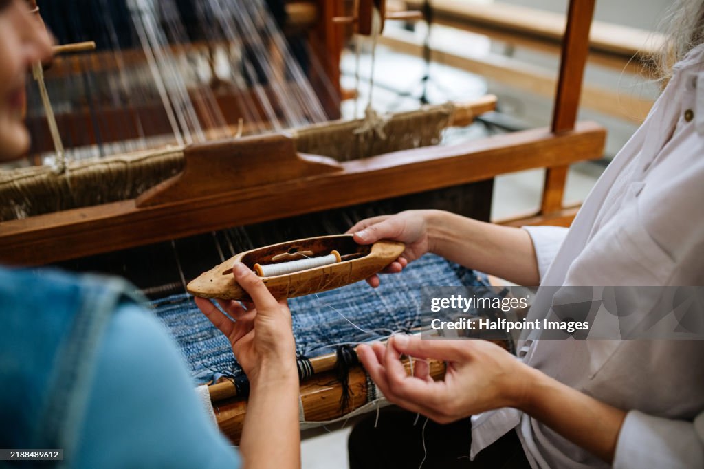 Mom teaching teenage girl to weave on wooden loom. Sustainable business, using recycled materials in fashion.