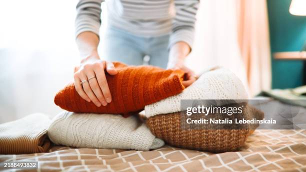sustainable living: a woman organizes her belongings at home, holding stacks of sweaters on a bed in her cozy bedroom, planning donations and mindful clothing purchases. banner - lana foto e immagini stock