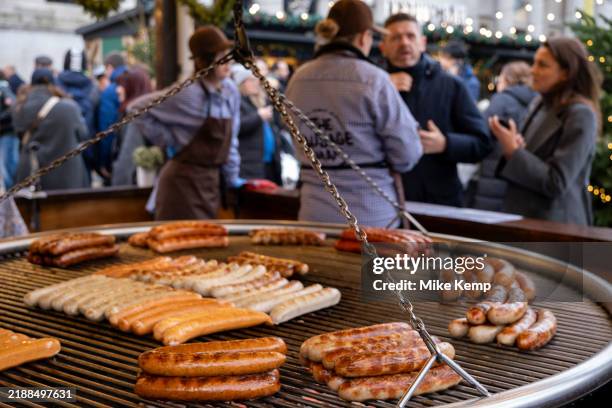 German bratwurst sausages on a large circular grill at a Christmas market stall on 2nd December 2024 in London, United Kingdom.