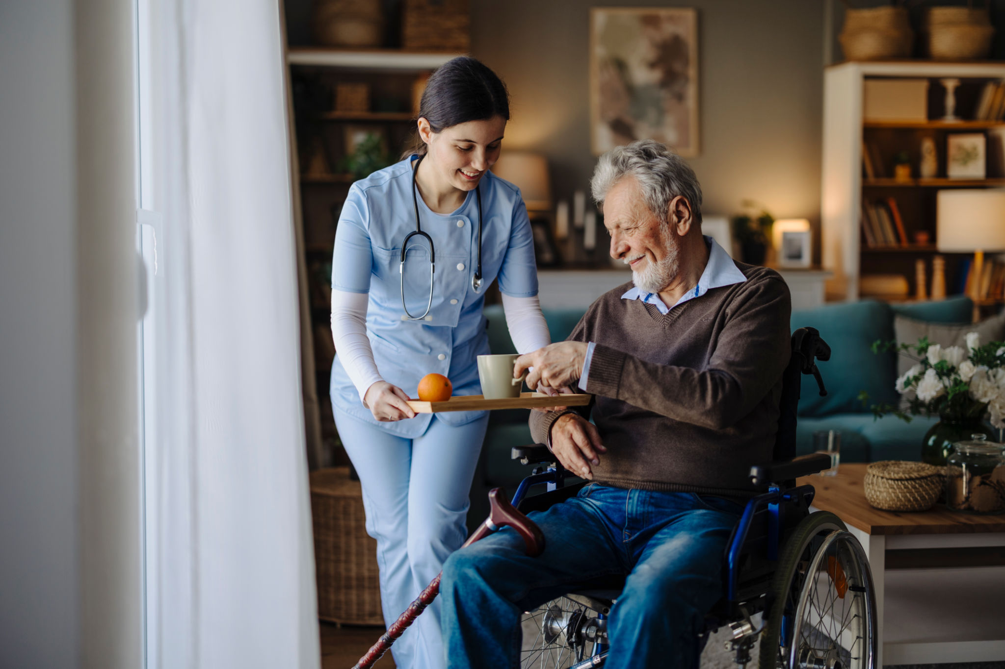 Senior man in wheelchair drinking tea in the nursing home assisted by the caregiver Senior man in wheelchair drinking tea in the nursing home assisted by the caregiver