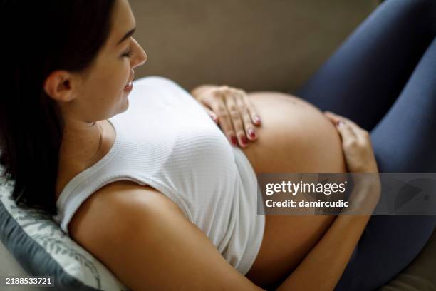 femme enceinte sereine allongée, profitant d’un moment de calme les mains sur son ventre rond - être enceinte photos et images de collection