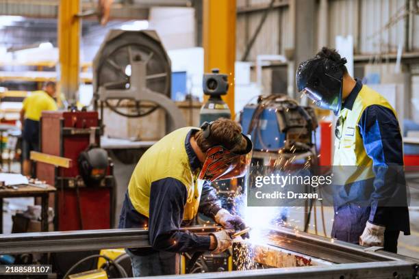 worker in protective gear welding metal in an industrial factory setting with sparks flying around brightly illuminating the area - lasser stockfoto's en -beelden