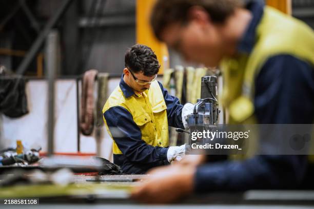 soudeurs qualifiés travaillant sur la construction en acier, meulant et soudant des pièces en fer dans un entrepôt moderne et lumineux - culture australienne photos et images de collection