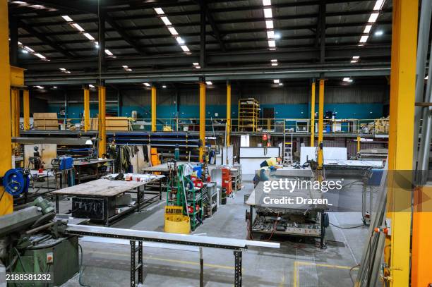 large industrial warehouse with machinery and yellow support structures under bright overhead lighting - fibreglass stock pictures, royalty-free photos & images