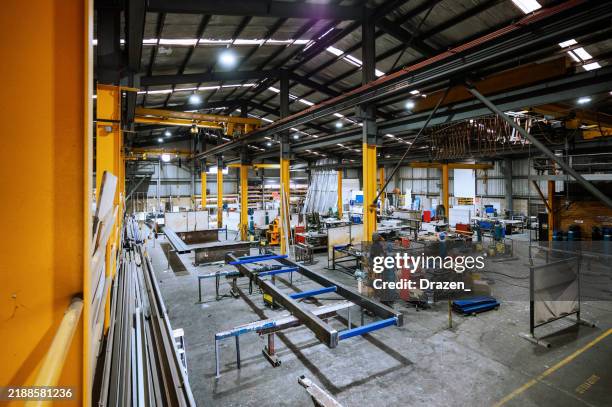 gran nave industrial con maquinaria y estructuras de soporte amarillas bajo una brillante iluminación cenital - fábrica fotografías e imágenes de stock