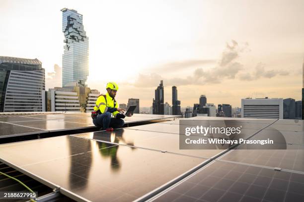 engineer analyzing solar panels on urban rooftop with laptop at sunset - energy transition stock pictures, royalty-free photos & images