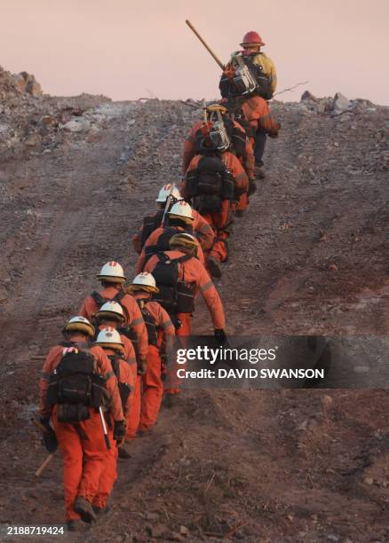 An inmate firecrew walks up a hill to battle the Franklin Fire as it grows in Malibu, California, on December 10, 2024. The fire tore through Malibu...