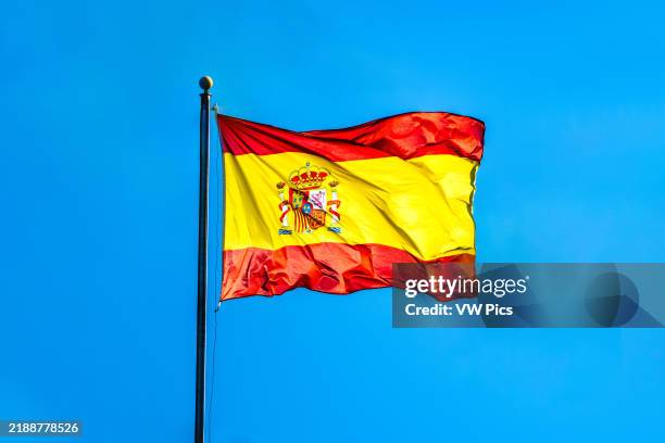 Spanish flag majestically waving against a clear blue sky in Seville, capturing a sense of national pride and vibrant culture.