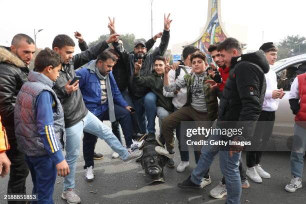 Syrians pose with a vandalized statue of Hafez al-Assad, father of Bashar al-Assad, in Umayyad Square on December 8, 2024 in Damascus, Syria. Rebel...