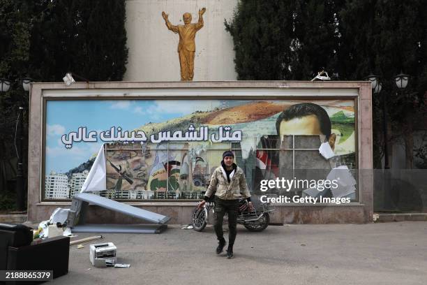 Man is pictured in front of a vandalized political banner featuring a portrait of Bashar al-Assad, following news the Syrian government regime had...