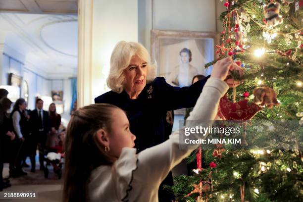 Britain's Queen Camilla and child place a decoration a Chritsmas tree during an event Clarence House, in London, on December 12, 2024 for children...