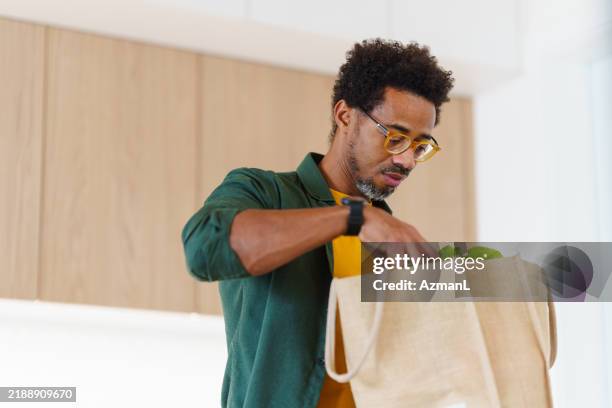 focused black male organizes groceries in modern kitchen - offloading stock pictures, royalty-free photos & images