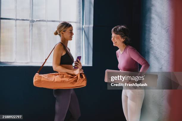 two women chatting at yoga studio with mats and bags - gym bag stock pictures, royalty-free photos & images