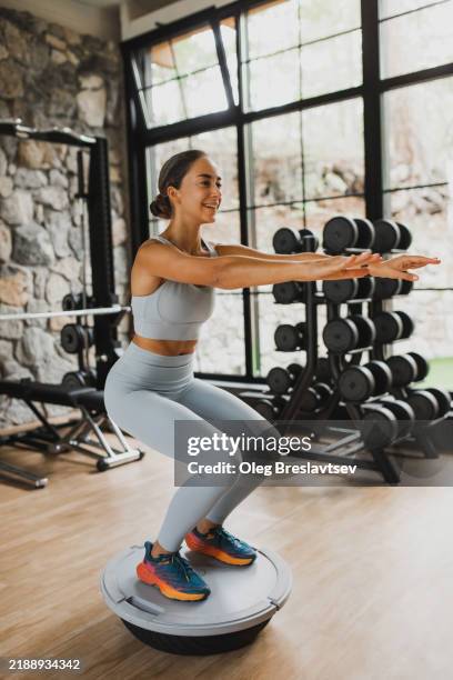 positive woman trying to keep balance when doing squats on balance board - bodyweight training stock pictures, royalty-free photos & images