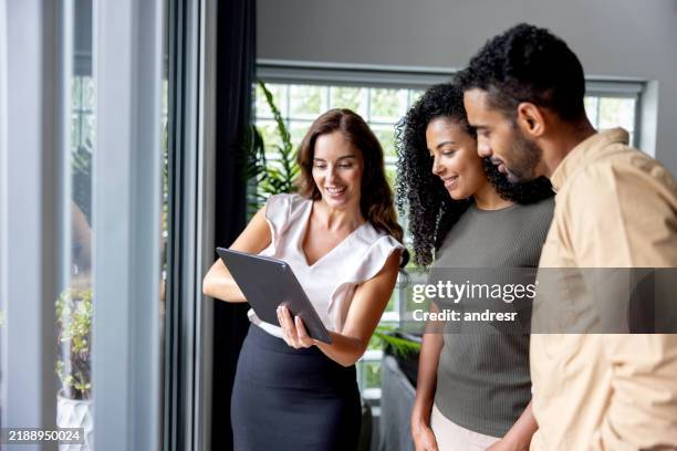 real estate agent showing couple pictures on a tablet while looking at a house for sale - landlord stock pictures, royalty-free photos & images