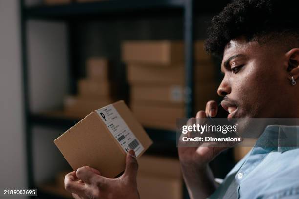 man looking a shipping label on a box and talking on the phone - parcel tracking stock pictures, royalty-free photos & images