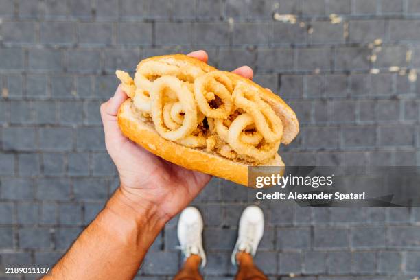 man eating bocadillo de calamares (calamari sandwich) on the street, personal perspective view - calamari stock pictures, royalty-free photos & images