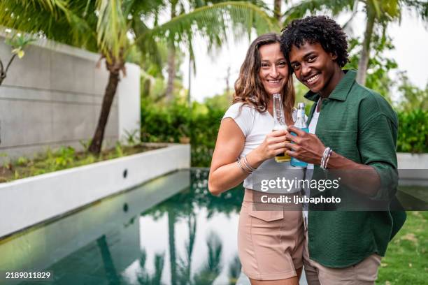 happy couple enjoying drinks by the pool on a sunny day - tropical tree stock pictures, royalty-free photos & images