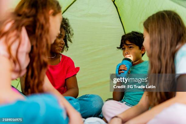 child friends telling stories using flashlight during camping - flashlight stockfoto's en -beelden