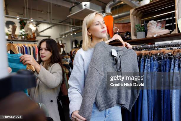 two young women shopping in a vintage charity shop - industrie de la mode photos et images de collection