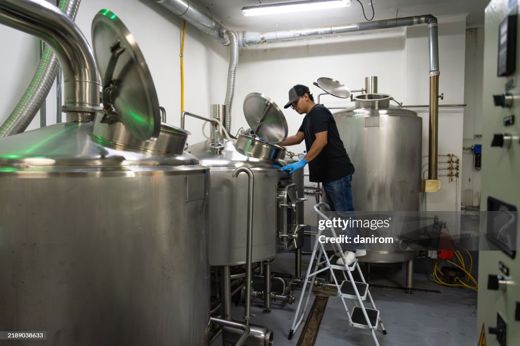 Worker inspecting stainless steel fermentation tanks in a brewery.
