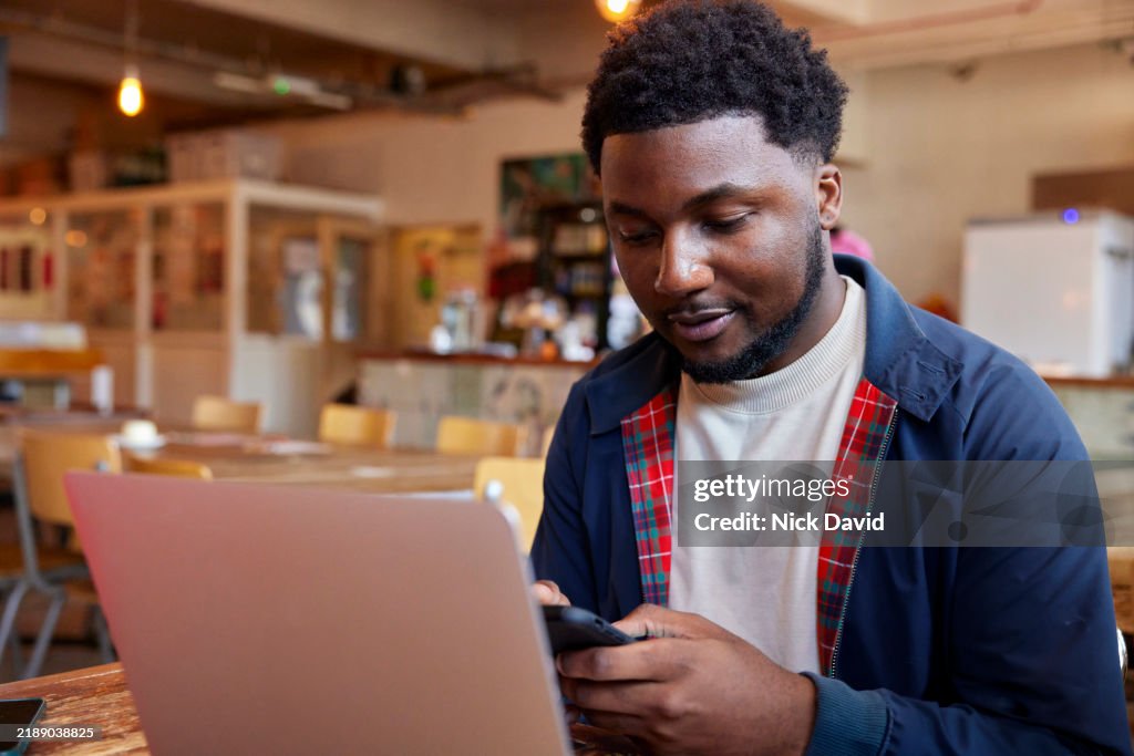 A young man text messaging on his mobile phone while working in a local cafe