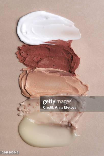 set of textured cosmetic smears smudged on beige background. moisturizing cream, cleansing facial mask, shower gel, exfoliating scrub and hair conditioner demonstrating pantone colored of the year 2025 - mocha mousse. - moka photos et images de collection