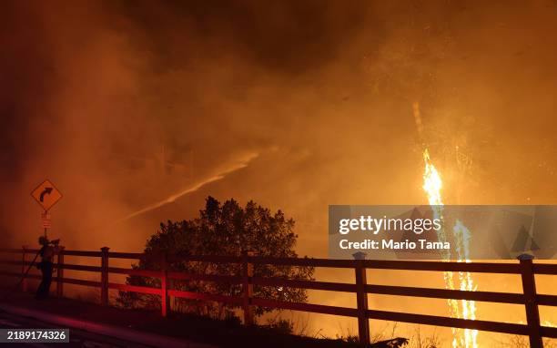 Firefighter sprays water as the Franklin Fire burns near a building on December 10, 2024 on Malibu, California. The wildfire has scorched 1,800 acres...